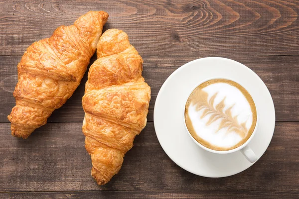 Koffiekopje en vers gebakken croissants op houten achtergrond. Boven — Stockfoto