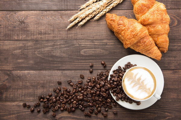 Coffee cup and fresh baked croissants on wooden background. Top 