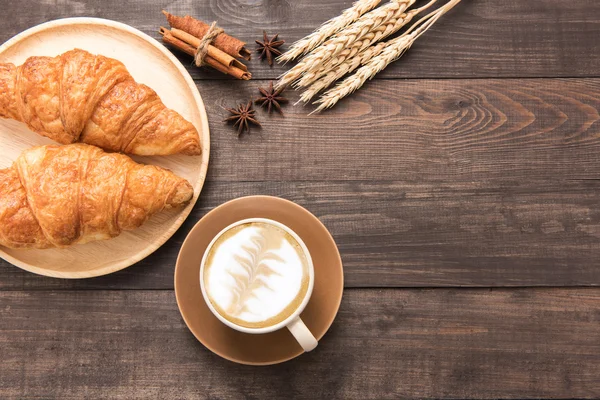 Koffiekopje en vers gebakken croissants op houten achtergrond. Boven — Stockfoto