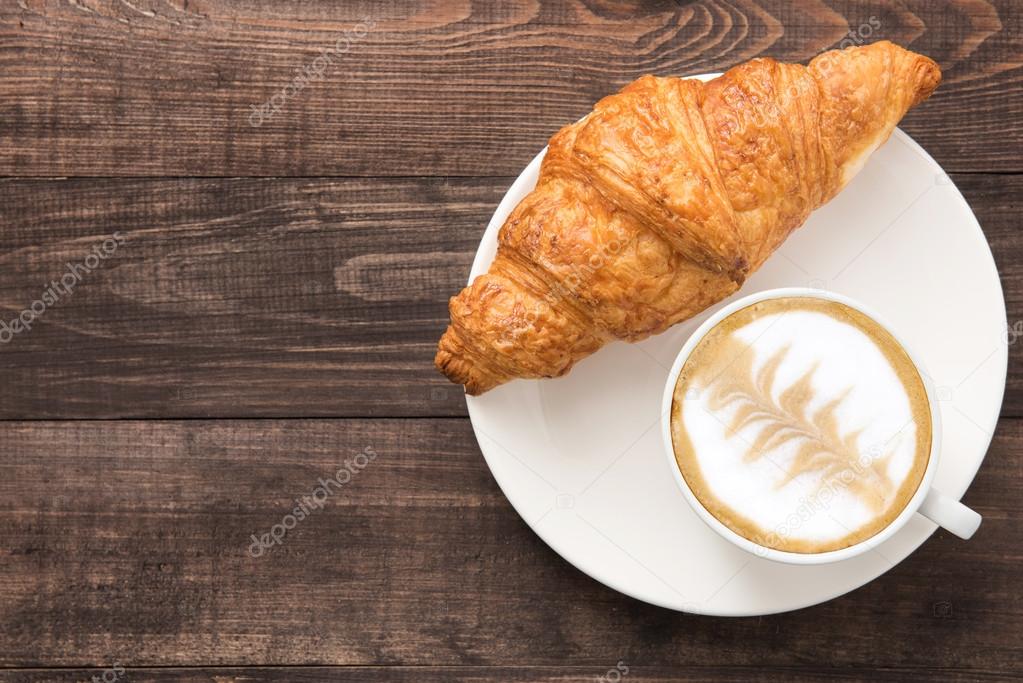 Coffee cup and fresh baked croissants on wooden background. Top 