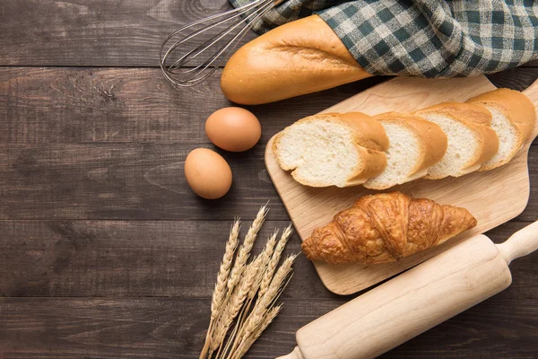 Frissen sült croissant, baguette és a tojás, a fából készült háttér — Stock Fotó