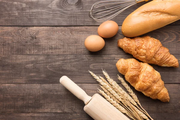 Frissen sült croissant, baguette és a tojás, a fából készült háttér — Stock Fotó