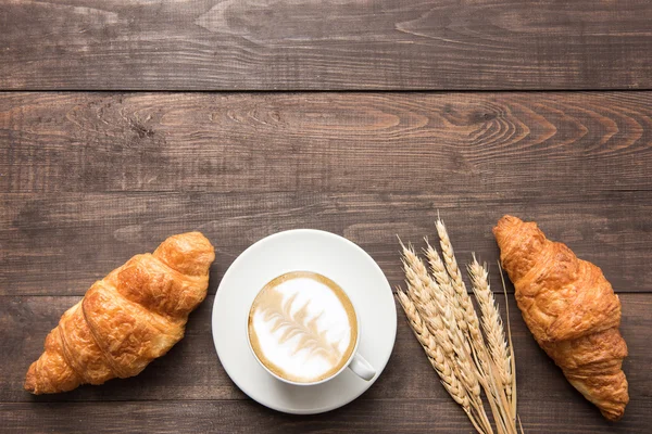 Koffiekopje en vers gebakken croissants op houten achtergrond. Boven — Stockfoto