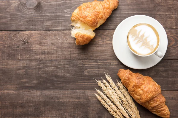 Taza de café y croissants recién horneados sobre fondo de madera. Parte superior — Foto de Stock