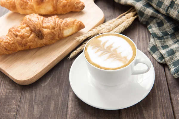 Snídaně šálek kávy a croissantu na dřevěné pozadí. — Stock fotografie