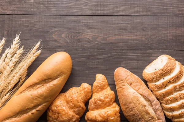 Čerstvě upečený chléb a pšenice na dřevěné pozadí — Stock fotografie