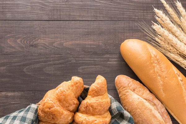 Pão fresco assado e trigo sobre fundo de madeira — Fotografia de Stock