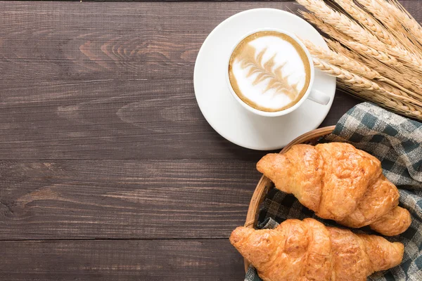 Koffiekopje en vers gebakken croissants op houten achtergrond. Boven — Stockfoto