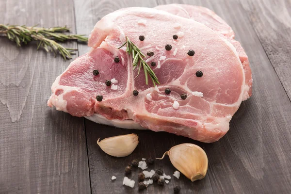 Roh geschnittenes Schweineschnitzel mit Knoblauch, Pfeffer auf Holzgrund — Stockfoto