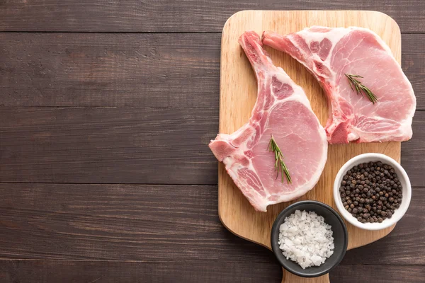 Horní pohled syrové vepřová kotleta steak a česnek, pepř na dřevěné pozadí — Stock fotografie