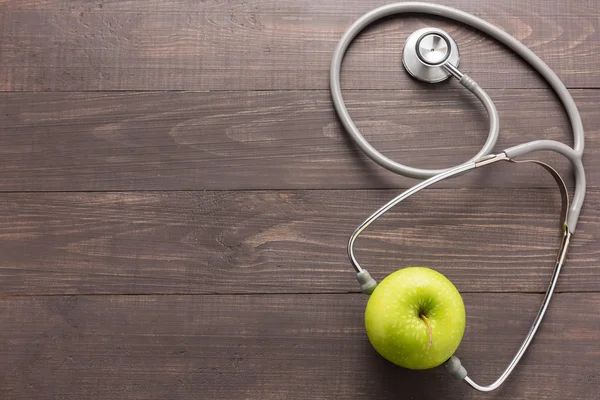 Concept voor gezondheidszorg, stethoscoop en groene appel op houten achtergrond. — Stockfoto