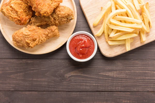 Gebakken kip en Franse frietjes op een houten achtergrond — Stockfoto