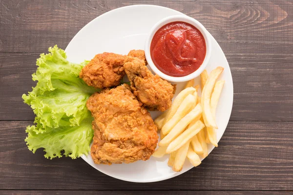 Gebakken kip en Franse frietjes op een houten achtergrond — Stockfoto