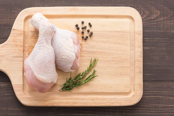 Baquetas de frango cru na placa de corte em fundo de madeira — Fotografia de Stock