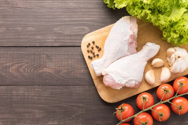 Ingredientes e perna de frango cru na placa de corte em backg de madeira — Fotografia de Stock