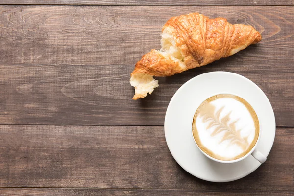 Koffiekopje en vers gebakken croissants op houten achtergrond. Boven — Stockfoto