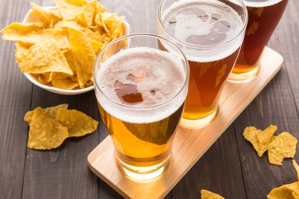 Surtido de vasos de cerveza con nachos fritos en una mesa de madera — Foto de Stock