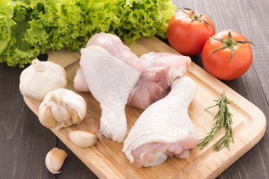 Malzemeler ve ahşap masa üzerinde kesme tahtası üzerinde çiğ tavuk budu