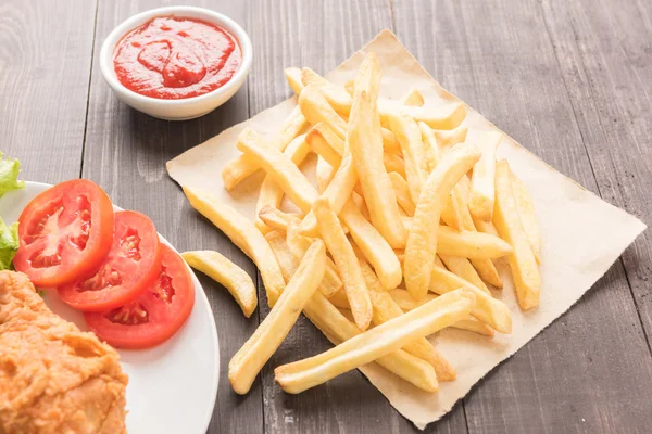 Pommes frites och stekt kyckling på ett träbord — Stockfoto