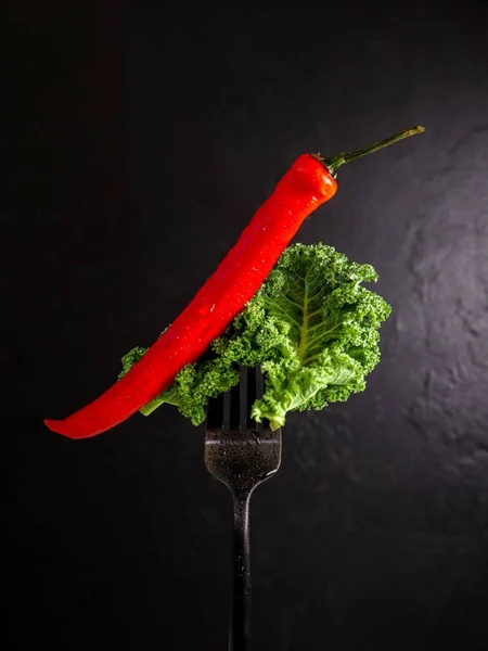 Kale with chilli pepper on a fork on black