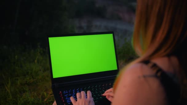 Young girl works at a laptop with a green screen on top of a mountain. — Stock Video