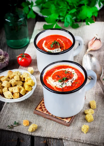 Kremalı domates çorbası kupalar ve yeşillik bir ahşap tablo.