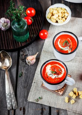 Kremalı domates çorbası kupalar ve yeşillik bir ahşap tablo.