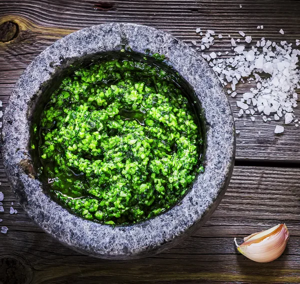 Pesto em argamassa de mármore, sal e alho sobre mesa de madeira . — Fotografia de Stock