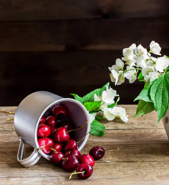 Cereja doce em caneca grande e flores em mesa de madeira . — Fotografia de Stock