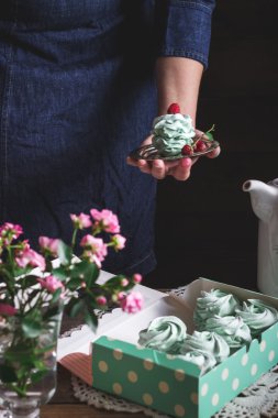 Ahududu kadın elinde, diğer meringues ahşap masa kutusunda dekore beze tatlısı. 