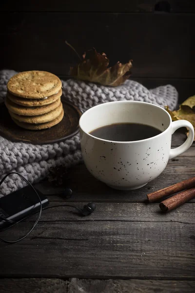 Чашка кофе / чая, печенье, опавшие листья, наушники и шарф на деревянном столе . — стоковое фото