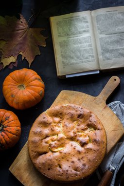 Koyu arka plan üzerine ev yapımı pasta kesme tahtası, kabak ve sonbahar yaprakları