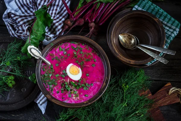 Russische koude soep met rode biet, bowl, lepels, groen op donkere houten tafel. Rustieke stijl. — Stockfoto