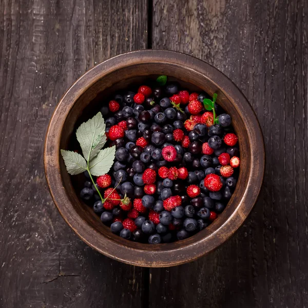 Koyu ahşap arka plan üzerinde yabani çilek ile kase.