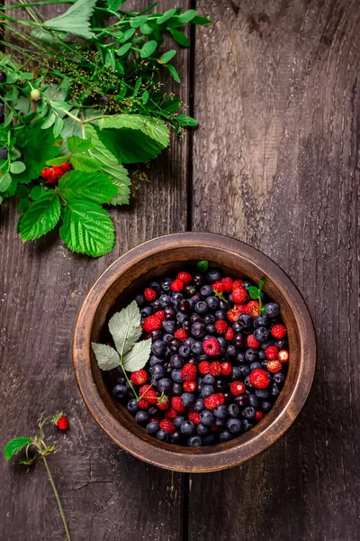 Wooden bowl with wild berries on dark wooden table.