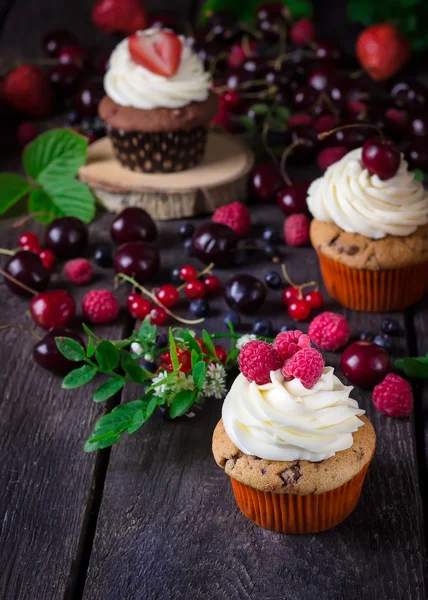 Cupcakes e bagas no fundo de madeira escura . — Fotografia de Stock