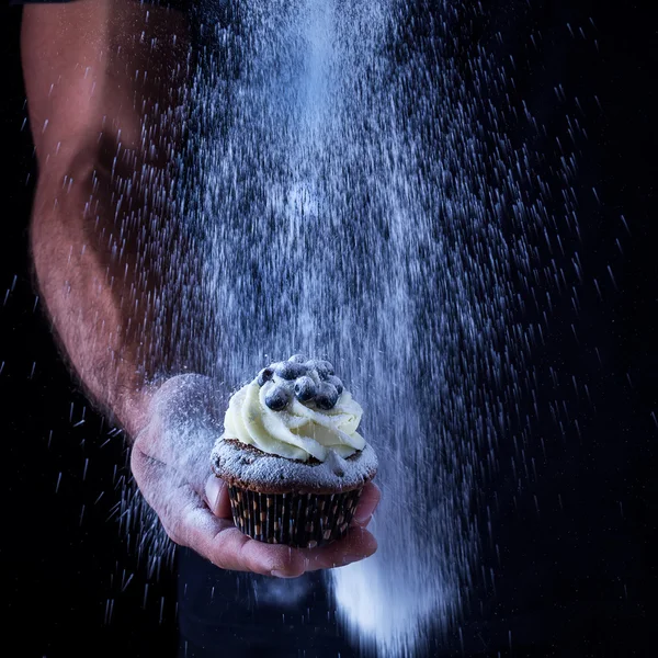 Cupcake en la mano de los hombres y el azúcar en polvo que vierte — Foto de Stock