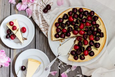 Kiraz lı cheesecake, tabaklar üzerinde iki dilim ve ahşap bir masada metal tepsi. .