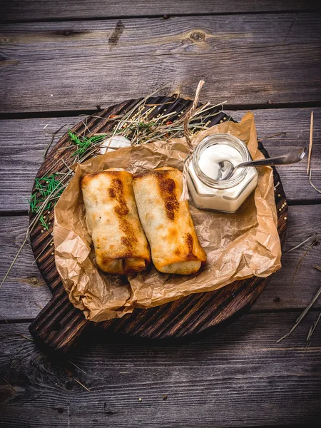 Pancakes with a stuffing and sour cream on a wooden table. — Stock Fotó