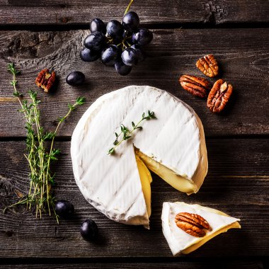 Cheese, herbs, nuts and grape on dark wooden table. Overhead view. clipart