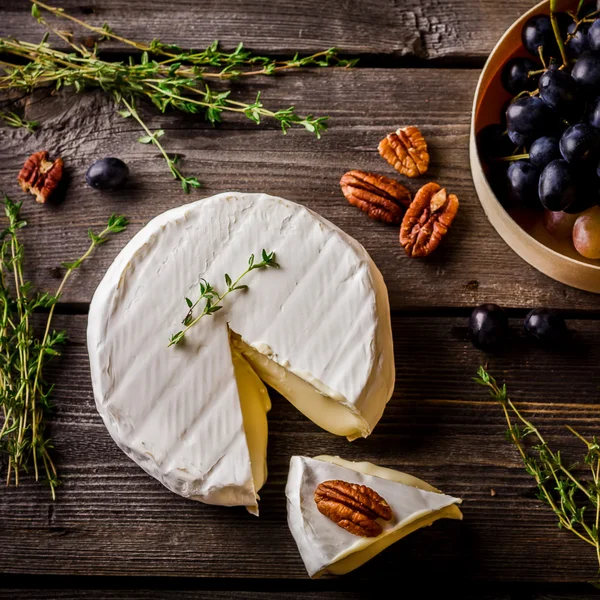 Käse, Kräuter, Nüsse und Trauben auf dunklem Holztisch. — Stockfoto