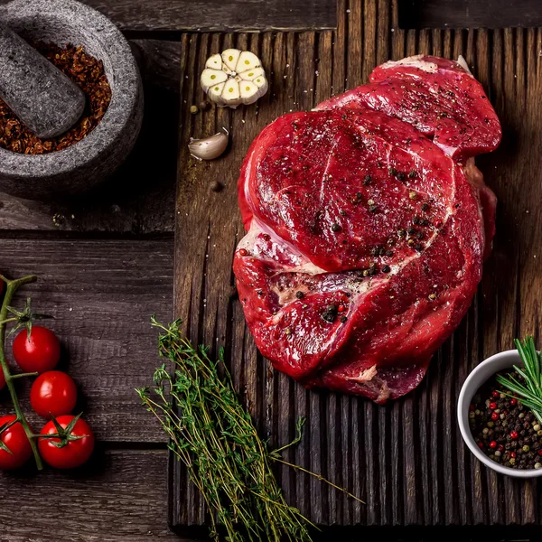  Bir doğrama tahtası, domates, otlar, sarımsak ve koyu ahşap masada baharat sığır eti .