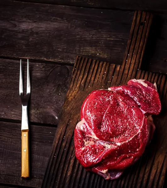 Carne de res en una tabla de cortar y tenedor en la mesa de madera oscura. Estilo rústico . — Foto de Stock