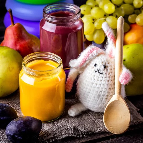 Baby food, fruits and bunny on wooden table.