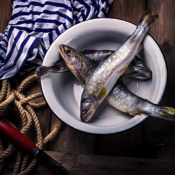 Raw river fish,knife and stripped vest on old wooden table. — Stock Photo, Image