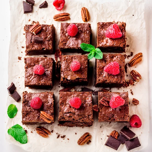 Pezzi di brownie con noci decorate con bacche e foglie di menta sulla carta bianca . — Foto Stock