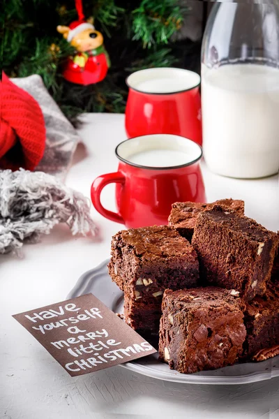 Pezzi di brownie con noci sul piatto, due tazze di latte e bottiglia. Albero di Natale . — Foto Stock