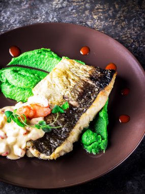 Seramik kahverengi plaka üzerinde soslu brokoli püresi ile balık.