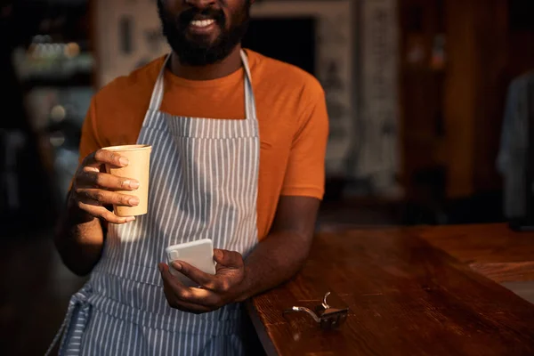 Peluquero sonriente usando smartphone y tomando café en el trabajo — Foto de Stock