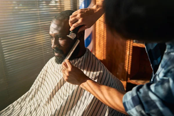 Barbeiro barbeando barba cliente na barbearia — Fotografia de Stock